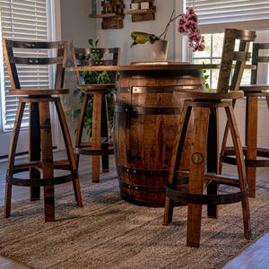 May include: A rustic bar set featuring a wooden barrel table and four matching swivel bar stools. The table and stools are made of dark-stained wood with metal accents. The set is placed on a neutral-colored rug.