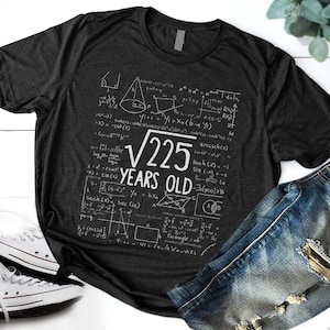 Peut inclure: Un t-shirt gris foncé avec un motif graphique blanc d'équations mathématiques et le texte "√225 YEARS OLD".
