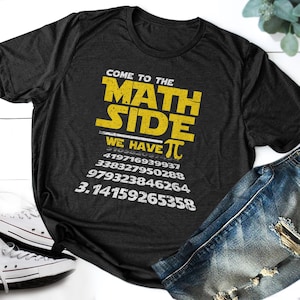 Puede incluir: Una camiseta gris oscura con un gráfico amarillo que dice "Come to the Math Side We Have Pi" e incluye los primeros 15 dígitos de pi.