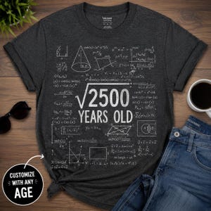 Op de afbeelding: Een donkergrijs t-shirt met korte mouwen en een witte grafische print van diverse wiskundige formules en vergelijkingen rondom de tekst "2500 YEARS OLD" met een wortelteken boven het getal 2500, op een Gildan-shirt.