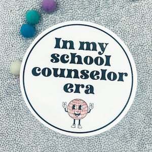 May include: White round sticker with black text that reads "In my school counselor era". A cartoon globe with a smiling face and peace signs is below the text.