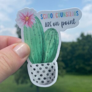 May include: A sticker with a watercolor illustration of a cactus in a black and white polka dot pot. The cactus has a pink flower and the text "SCHOOL COUNSELORS ARE ON POINT" in rainbow colors.