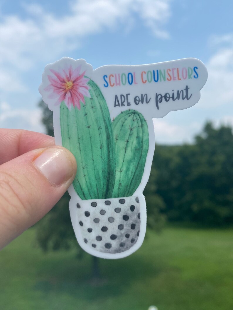 May include: A sticker with a watercolor illustration of a cactus in a black and white polka dot pot. The cactus has a pink flower and the text "SCHOOL COUNSELORS ARE ON POINT" in rainbow colors.