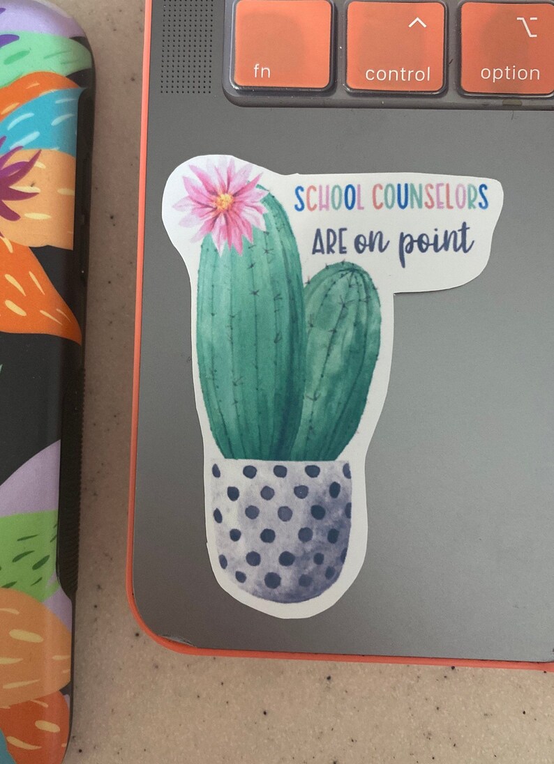May include: A sticker with a watercolor illustration of two cacti in a pot with black polka dots. The cacti are green and have pink flowers. The text on the sticker reads "School Counselors Are on Point".