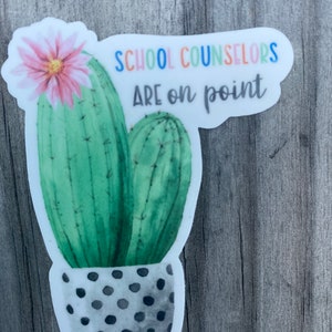 May include: A sticker with a watercolor illustration of a cactus in a polka dot pot. The text "SCHOOL COUNSELORS ARE on point" is written in rainbow colors above the cactus.