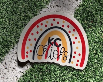 May include: A red, yellow, and black rainbow sticker with white polka dots. The sticker says "KC Chiefs" in black lettering.