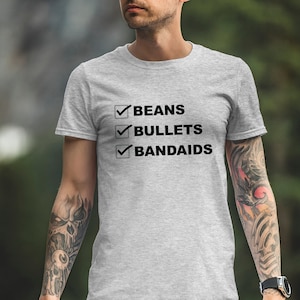 May include: A gray t-shirt with a checklist on the front. The checklist includes the items "Beans", "Bullets", and "Bandaids", all with checkmarks next to them.