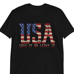 Pu&ograve; includere: Maglietta nera con un design di bandiera americana usurato che recita "USA LOVE IT OR LEAVE IT".