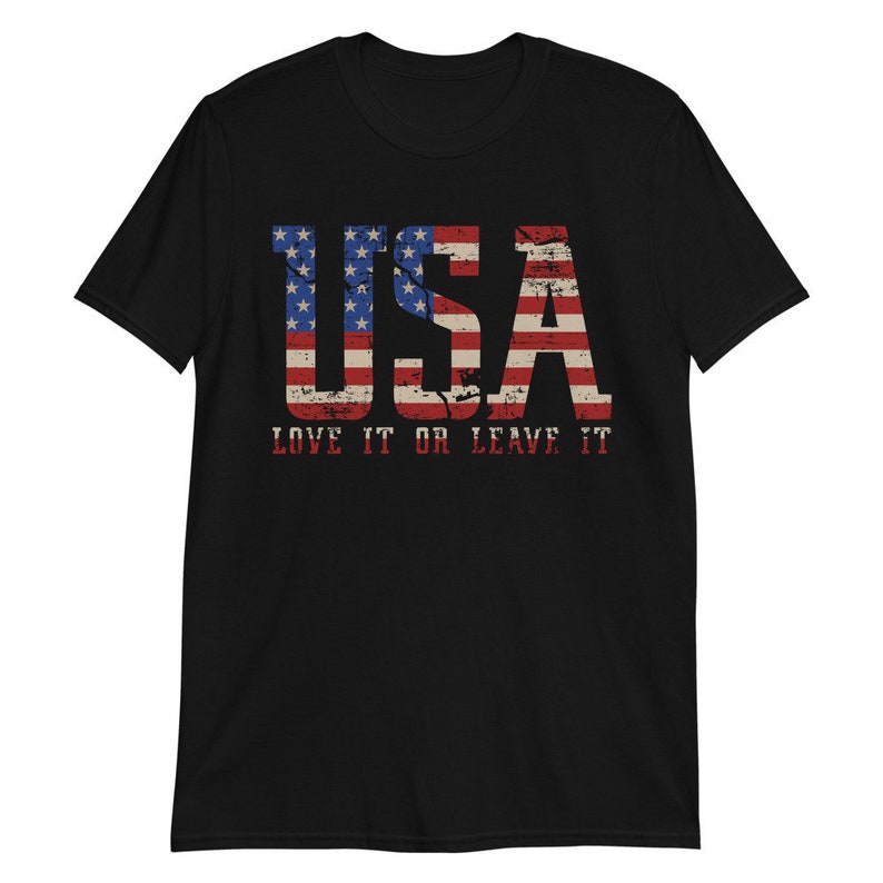 Pu&ograve; includere: Maglietta nera con un design di bandiera americana usurato che recita "USA LOVE IT OR LEAVE IT".