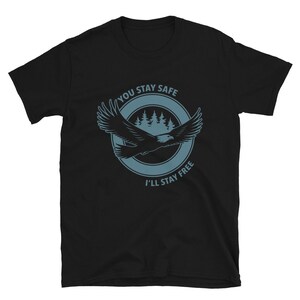 K&ouml;nnte beinhalten: Schwarzes T-Shirt mit einer blauen Grafik eines im Flug befindlichen Adlers mit dem Text "You Stay Safe I'll Stay Free" in einem Kreis darum.
