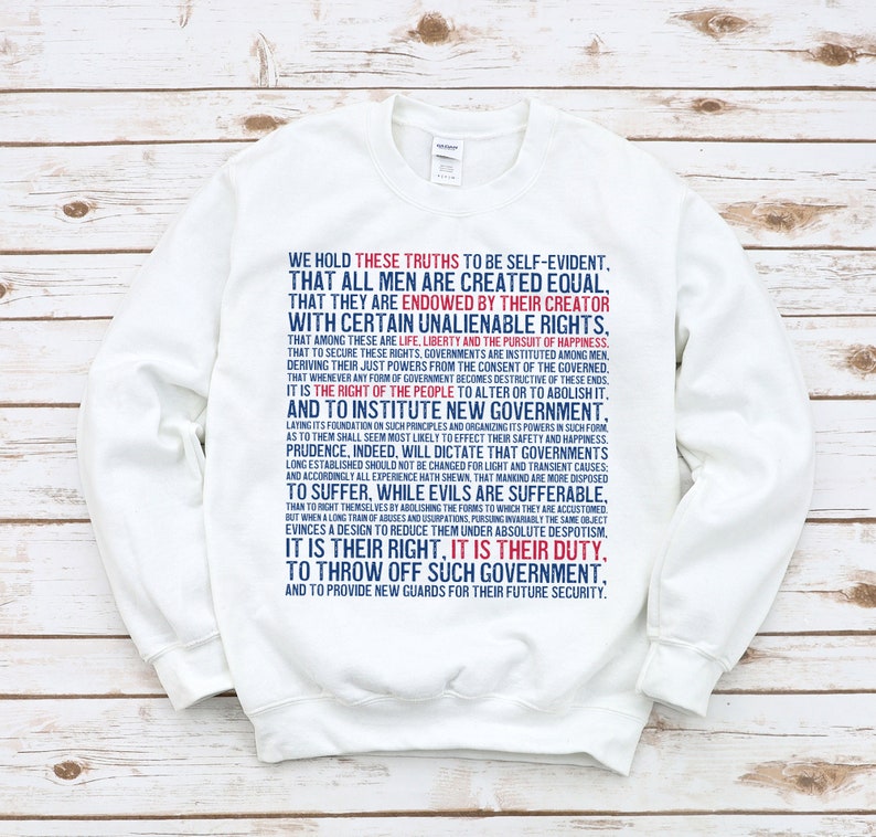 May include: White sweatshirt with a blue and red text print of the Declaration of Independence. The text reads "We hold these truths to be self-evident..."