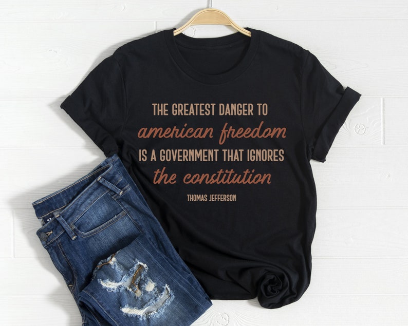 May include: Black t-shirt with a quote by Thomas Jefferson in brown text: "The greatest danger to american freedom is a government that ignores the constitution."