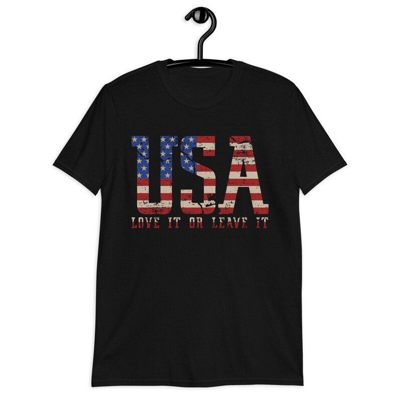 Pu&ograve; includere: Maglietta nera con un design di bandiera americana usurato che recita "USA LOVE IT OR LEAVE IT".