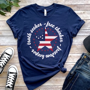 Puede incluir: Una camiseta azul marino con un dise&ntilde;o de estrella blanca y el texto "truth seeker - free thinker - freedom keeper".
