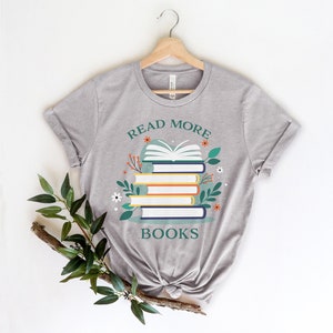 May include: A gray t-shirt with the text "Read More Books" and a stack of books with flowers and leaves around them.