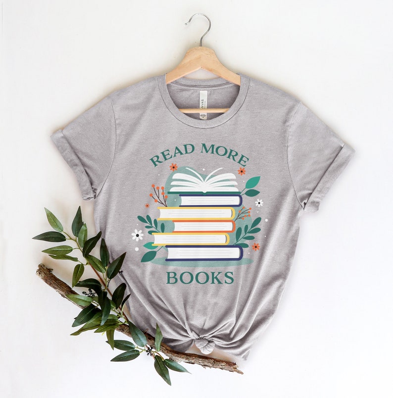 May include: A gray t-shirt with the text "Read More Books" and a stack of books with flowers and leaves around them.