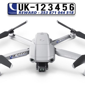 Op de afbeelding: Een witte DJI Mavic Air 2 drone met zwarte propellers. De drone heeft een sticker aan de zijkant met de tekst "UK-123456" en "REWARD - 353 871 044 518".