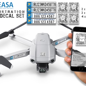 Puede incluir: Un dron blanco con hélices negras y una pegatina de registro EASA azul y blanca. La pegatina incluye el número de registro IRL123WKD456T78 y el texto "IF FOUND PLEASE CONTACT 086 123 4567". El dron está siendo escaneado por un teléfono inteligente con un código QR.