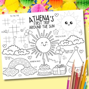 May include: A black and white activity sheet with the text "ATHENA'S FIRST TRIP AROUND THE SUN". The sheet includes a tic-tac-toe grid, a rainbow maze, and a sun with a smiling face. Colored pencils are in the bottom right corner.