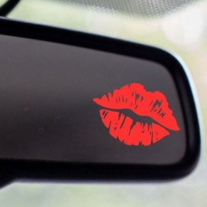 May include: A red lip print sticker on a black car rearview mirror.