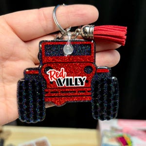 May include: Red glitter Jeep keychain with a black tassel. The Jeep has the words "Red Willy" on the front.