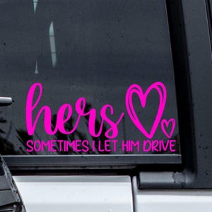 May include: A pink car decal with the word "hers" in cursive, followed by a heart symbol. Below, the text reads "SOMETIMES I LET HIM DRIVE". The decal is designed to be applied to a car window.