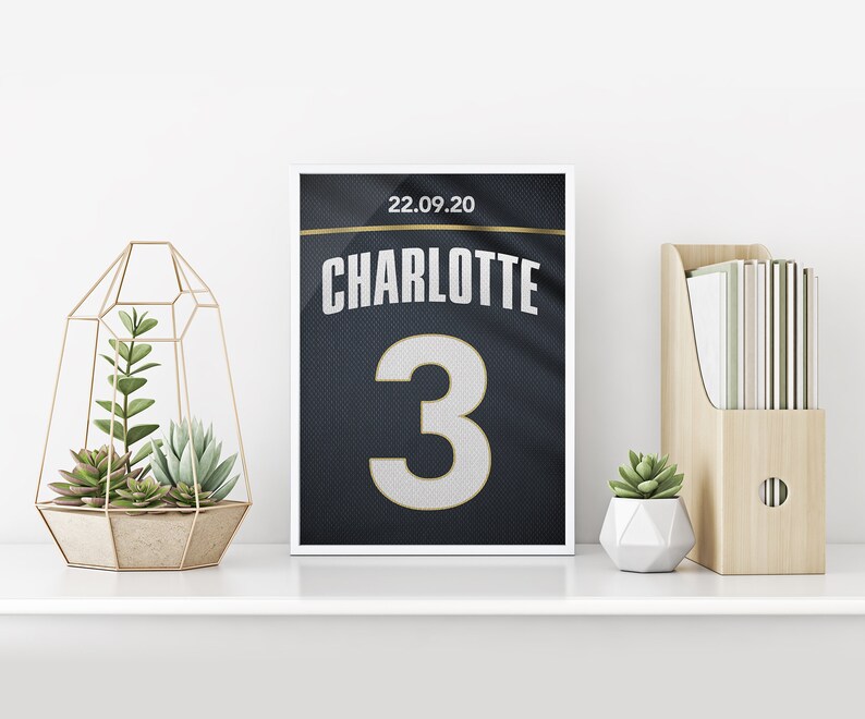 May include: A framed print of a black and gold jersey with the name "CHARLOTTE" and the number "3" on it. The date "22.09.20" is printed above the name.