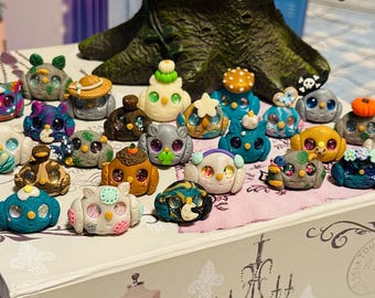 Puede incluir: Colección de figuras de búhos coloridos y hechos a mano. Cada búho presenta detalles únicos, como sombreros y flores. Los búhos se exhiben en una caja decorativa, mostrando una variedad de colores y diseños.