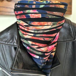 May include: A black leather jacket with a floral print neck gaiter. The neck gaiter features a blue background with pink and orange flowers and black horizontal stripes. The jacket has a silver zipper.