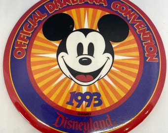 May include: A red, white, and blue circular pin with a cartoon image of Mickey Mouse. The text "OFFICIAL DISNEYANA CONVENTION 1993 DISNEYLAND" is printed around the edge of the pin.