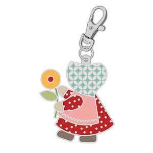 May include: A metal keychain charm featuring a cartoon figure of a woman in a red polka-dot dress and pink apron, holding a yellow flower. The charm has a silver clasp for easy attachment.