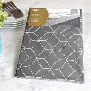 May include: A gray PVC tablecloth with a white geometric pattern, packaged in clear plastic. The label reads "GEO FLOW PVC TABLECLOTH". The tablecloth is shown with a stack of white plates, silverware, and a small vase with greenery.