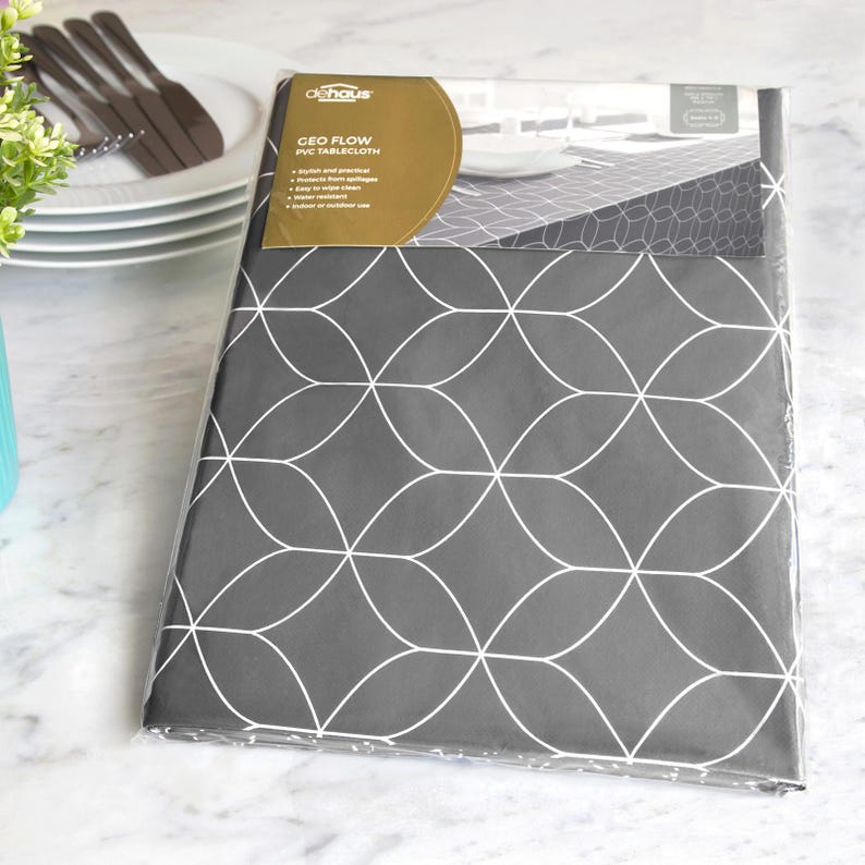 May include: A gray PVC tablecloth with a white geometric pattern, packaged in clear plastic. The label reads "GEO FLOW PVC TABLECLOTH". The tablecloth is shown with a stack of white plates, silverware, and a small vase with greenery.
