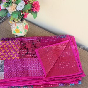 May include: A pink kantha quilt with a patchwork design. The quilt is folded in half and has a floral pattern on the fabric. The quilt is made of cotton and is hand-stitched.
