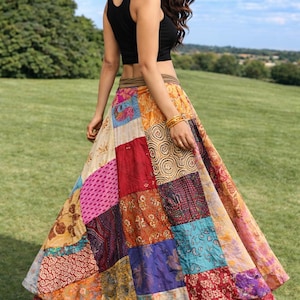 May include: A woman wearing a black crop top and a patchwork skirt. The skirt is made of various colorful fabrics, including pink, red, blue, and gold. The skirt has a layered design and a flowing silhouette.