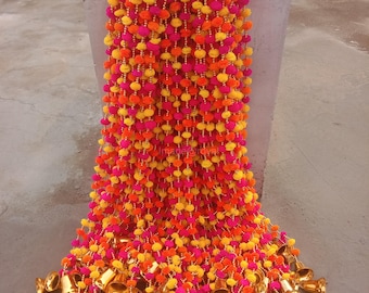 May include: A long garland of pink, orange, and yellow pom-poms with gold bells hanging from the bottom.