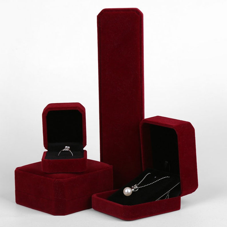 Peut inclure: Trois bo&icirc;tes &agrave; bijoux en velours rouge. La plus grande bo&icirc;te est haute et rectangulaire. Les deux autres bo&icirc;tes sont carr&eacute;es et ont des couvercles. Une bo&icirc;te contient une bague et l'autre contient un collier avec un pendentif en perle.