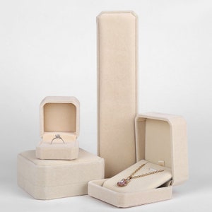 Peut inclure: Trois bo&icirc;tes &agrave; bijoux en velours beige. La plus grande bo&icirc;te est haute et rectangulaire. La bo&icirc;te du milieu est carr&eacute;e et contient une plus petite bo&icirc;te carr&eacute;e &agrave; l'int&eacute;rieur. La plus petite bo&icirc;te est carr&eacute;e et contient un collier &agrave; l'int&eacute;rieur.