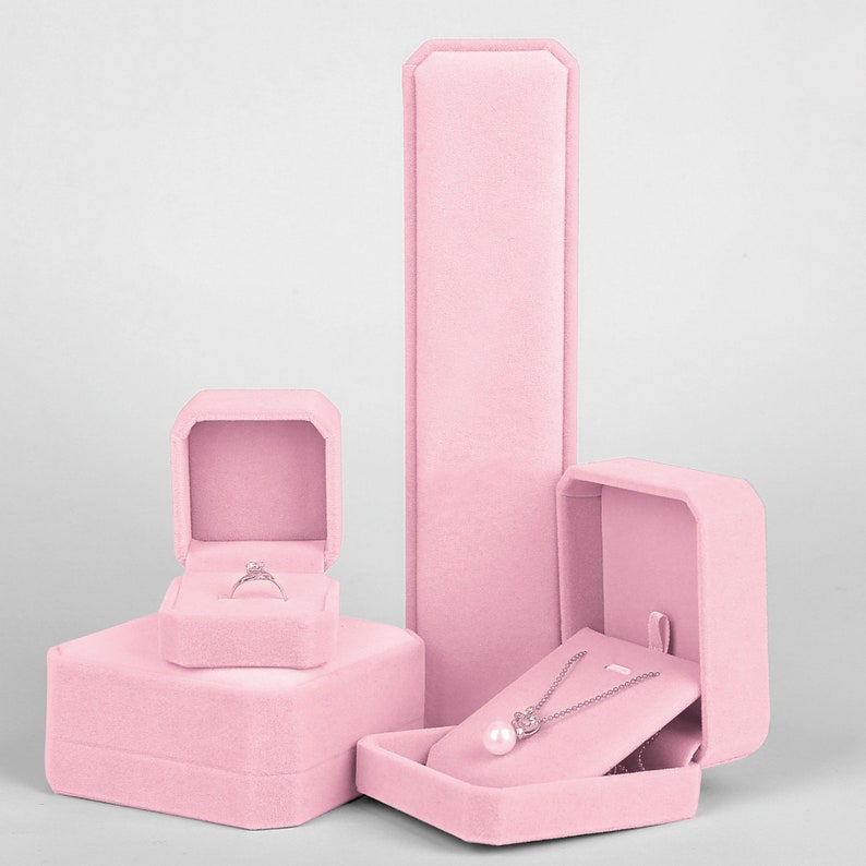 Peut inclure: Trois bo&icirc;tes &agrave; bijoux en velours rose. La plus grande bo&icirc;te est rectangulaire et a un couvercle qui s'ouvre pour r&eacute;v&eacute;ler un collier. La bo&icirc;te du milieu est carr&eacute;e et a un couvercle qui s'ouvre pour r&eacute;v&eacute;ler une bague. La plus petite bo&icirc;te est carr&eacute;e et a un couvercle qui s'ouvre pour r&eacute;v&eacute;ler une bague.