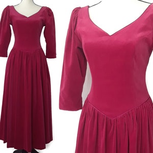 May include: A long, deep pink velvet dress with a V-neckline and 3/4 sleeves. The dress has a fitted bodice and a full skirt.