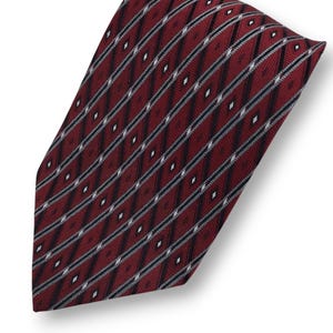 May include: A maroon tie with a diagonal pattern of black, white, and gray stripes and diamond shapes. The tie is folded over on a white background.