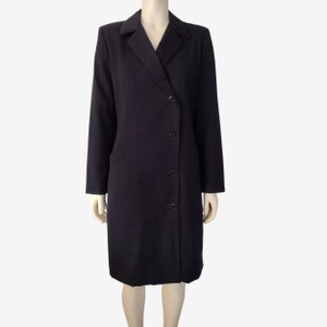 May include: A long-sleeved black dress with a collar and a button-up front. The dress has a single pocket on the left side and a slightly asymmetrical hemline.