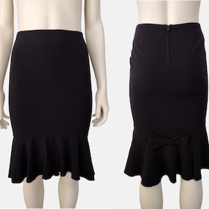 May include: Black skirt with a fitted silhouette and a ruffled hem. The skirt has a bow detail at the back.