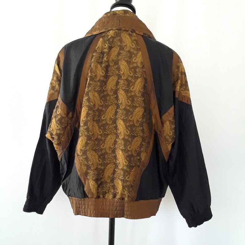 Peut inclure: Une veste noire et marron avec un motif paisley au dos. La veste a une fermeture &eacute;clair et un col montant.