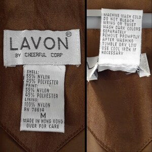 Peut inclure: Une &eacute;tiquette blanche avec le texte "LAVON BY CHEERFUL CORP" et une &eacute;tiquette d'entretien avec des instructions pour laver et s&eacute;cher le v&ecirc;tement. L'&eacute;tiquette d'entretien indique "MACHINE WASH COLD, DO NOT BLEACH, WRING OR TWIST, WASH DARK COLORS SEPARATELY, REMOVE PROMPTLY AFTER WASHING, TUMBLE DRY LOW, USE COOL IRON IF NECESSARY". L'&eacute;tiquette de composition du tissu indique "SHELL: 55% NYLON 45% POLYESTER, PRINT: 55% NYLON 45% POLYESTER, LINING: 100% NYLON, RN 78614, M, MADE IN HONG KONG, OVER FOR CARE".