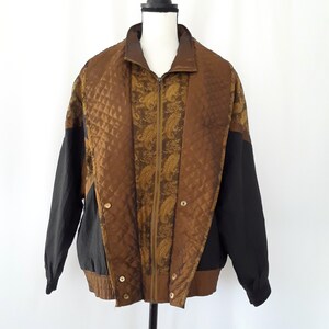 Peut inclure: Une veste r&eacute;versible noire et marron avec un motif matelass&eacute; et un motif paisley. La veste a une fermeture &eacute;clair et un col montant.