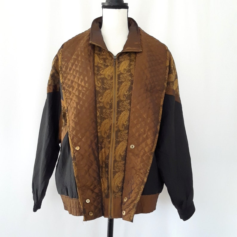 Peut inclure: Une veste r&eacute;versible noire et marron avec un motif matelass&eacute; et un motif paisley. La veste a une fermeture &eacute;clair et un col montant.