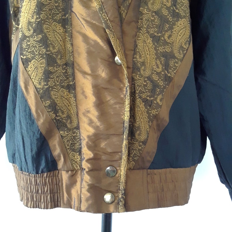 Peut inclure: Une veste bomber noire et dor&eacute;e &agrave; motif paisley. La veste a une fermeture &eacute;clair et un col montant.