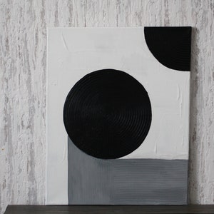Può includere: Dipinto astratto su tela con cerchi neri e una forma geometrica grigia su sfondo bianco.