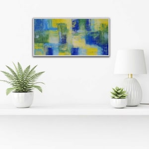 May include: Abstract painting with a mix of blue, green, and yellow colors. The painting is framed in a silver frame and is hanging on a white wall.